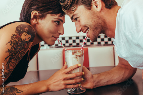 Romantic couple sharing milk shake using straws from the same gl photo