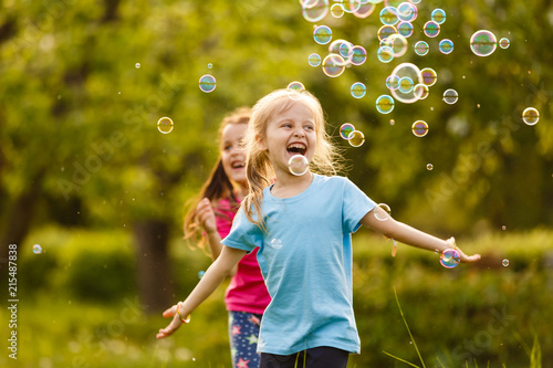 Two Little girl fun with soap bubbles in summer park  green fields  nature background  spring season