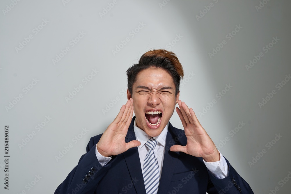 young Asian business man shouting with hands cupped to his mouth, isolated on gray background young Asian business man shouting with hands cupped to his mouth, isolated on gray background