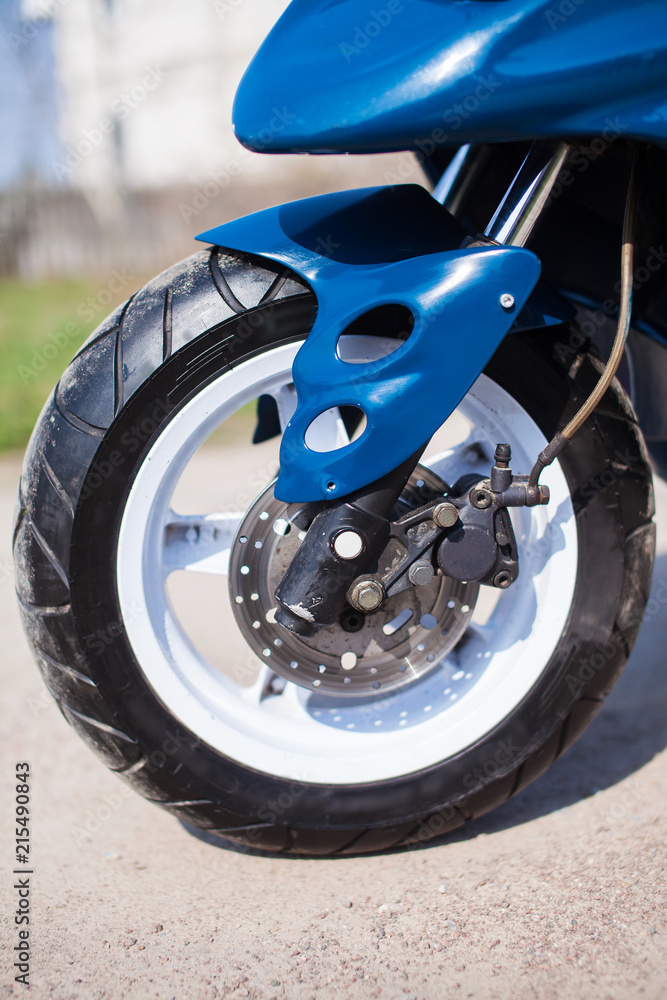 Obraz premium Front wheel of blue modern scooter on the gravel road