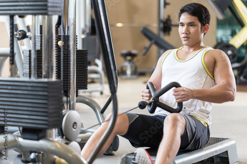 Portrait of a determined handsome young man looking forward while rowing at the cable machine during workout for back muscles in a modern fitness club