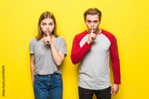 Young couple smiling with silence gesture or keep secret on a yellow background