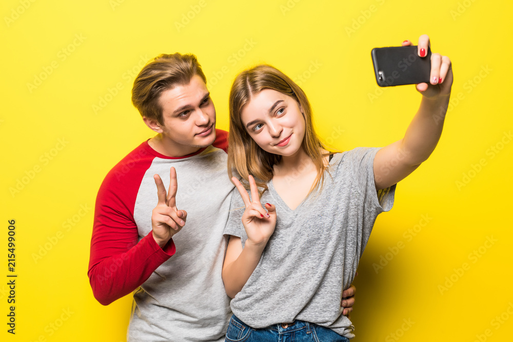 Young lovely couple posing together while making selfie on smartphone over yellow background Young lovely couple posing together while making selfie on smartphone over yellow background