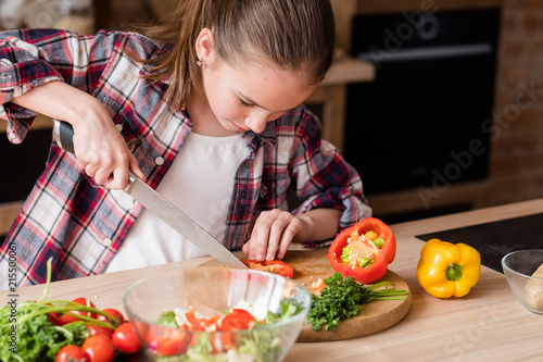 little cook. adolescent girl cutting vegetables and preparing dinner from fresh organic food ingredients. healthy eating and wholesome nutrition concept.