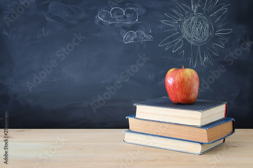 back to school concept. stack of books and apple over wooden desk in front of blackboard.