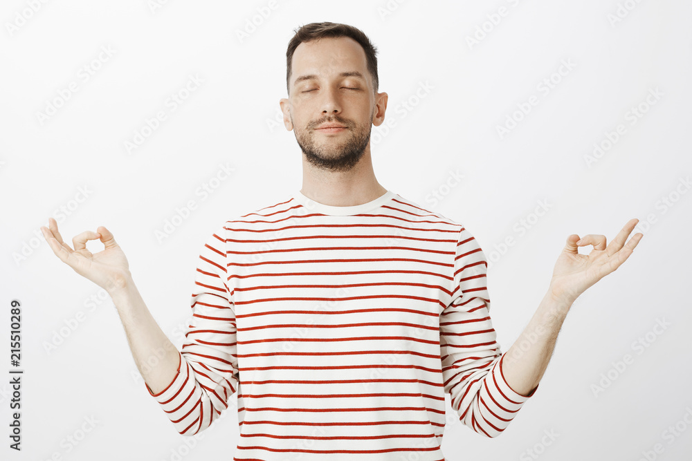 Trying to find peace inside body. Portrait of calm relaxed handsome husband, closing eyes and spreading hands aside with zen gesture, meditating or practicing yoga over gray background Trying to find peace inside body. Portrait of calm relaxed handsome husband, closing eyes and spreading hands aside with zen gesture, meditating or practicing yoga over gray background