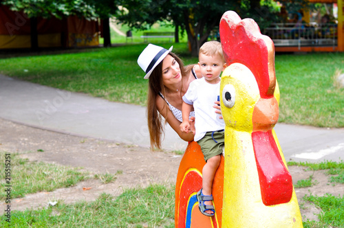 A young cheerful mother plays with her child in the playground where there is a chicken sculpture