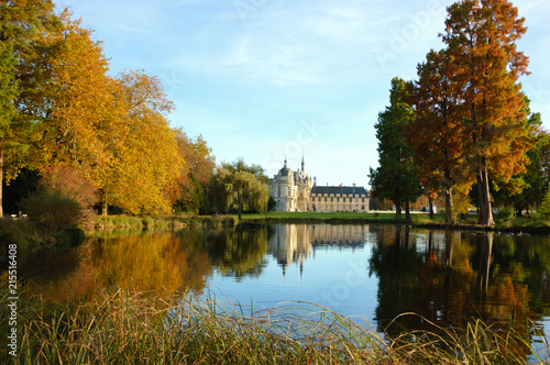 View of Chantilly castle reflected in pool surrounded by park trees. Autumn. France.