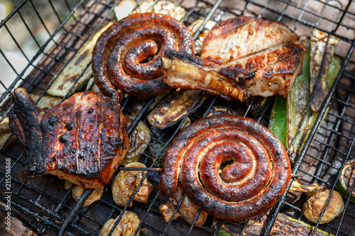 Twisted sausages, pork steak, mushrooms and zucchini cooked on grill.