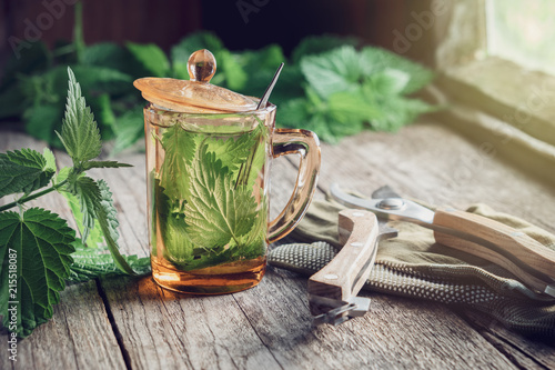 Foto Nettle tea or infusion, nettle plants and garden pruner on wooden table in a village house