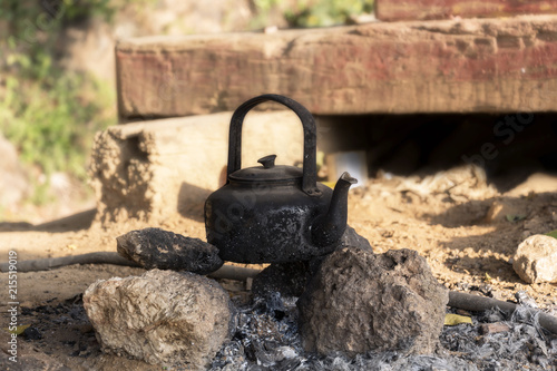 Classic old kettle with black soot on pile of stones at camping with nature background.