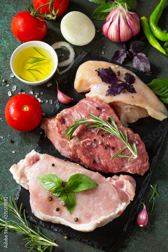 Fresh raw meat. Different types of raw pork meat, chicken fillet and beef with vegetables and herbs on dark wooden background.