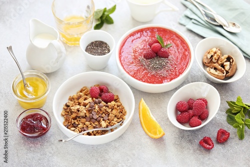 Breakfast table setting with granola, smoothy bowl and fresh raspberries. Overhead view