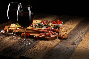 Italian antipasti wine snacks set. Cheese variety, Mediterranean olives, crudo, Prosciutto di Parma, salami and wine in glasses over wooden grunge background.
