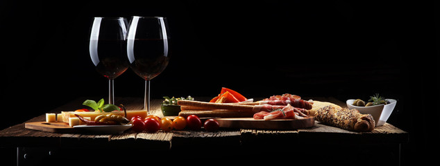 Italian antipasti wine snacks set. Cheese variety, Mediterranean olives, crudo, Prosciutto di Parma, salami and wine in glasses over wooden grunge background.