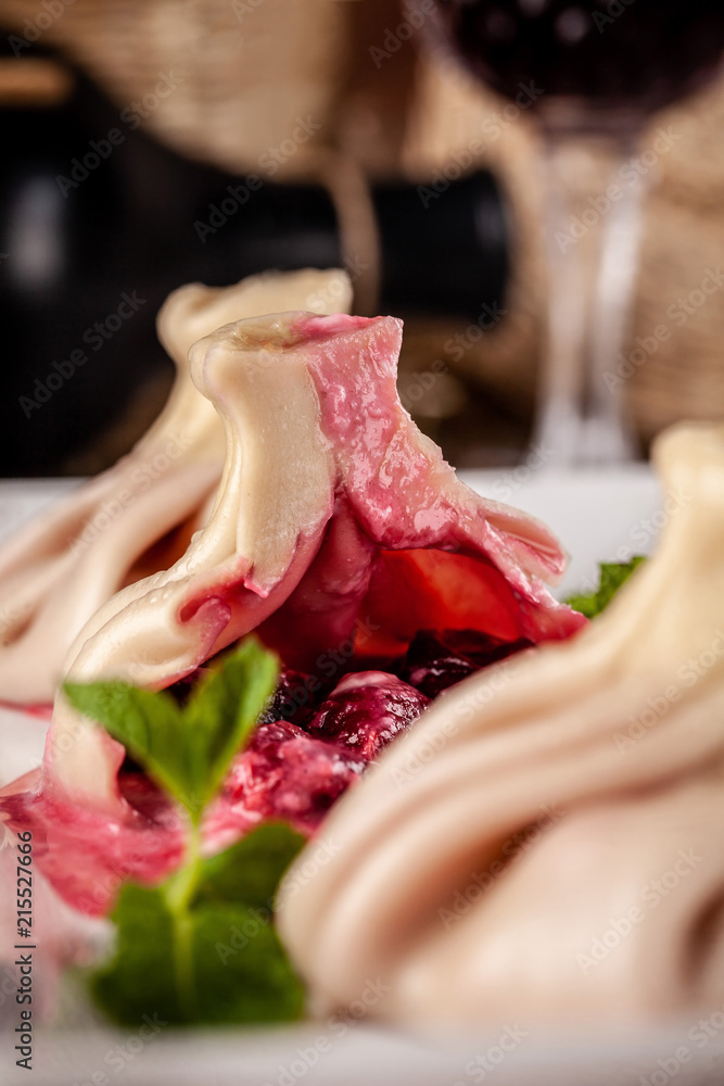 Traditional Georgian and Armenian cuisine. Georgian khinkali with a cherry on a white plate, on a wooden table in a restaurant. Wine on the table. Copy space, selective focus Traditional Georgian and Armenian cuisine. Georgian khinkali with a cherry on a white plate, on a wooden table in a restaurant. Wine on the table. Copy space, selective focus