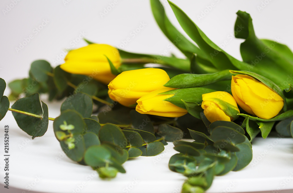 Obraz premium beautiful yellow tulips with eucalyptus branches on a white table
