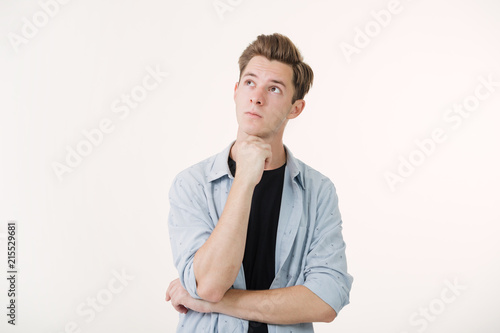 Pensive handsome young man wearing blue shirt over white background © Leika production