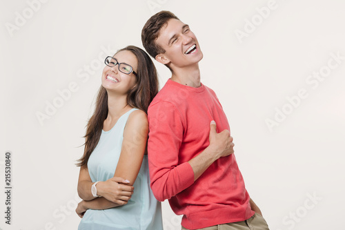 Happy young lovely couple standing back to back and laughing over white background. Friendship and relationships