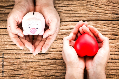 Man and women hand hold a piggy bank and red heart with copy space on old wood background, Health insurance concept.