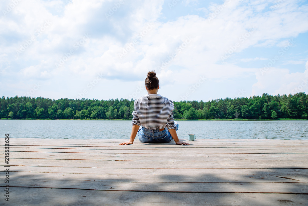 woman sitting on wooden dock looking at lake in sunny day