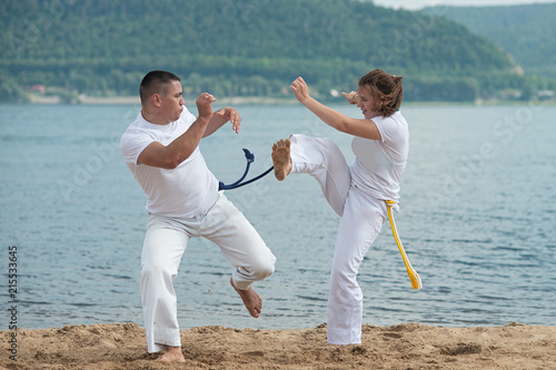 Man and woman train capoeira on the beach - concept about people, lifestyle and sport.