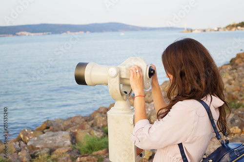 The girl looks through the telescope at the sea