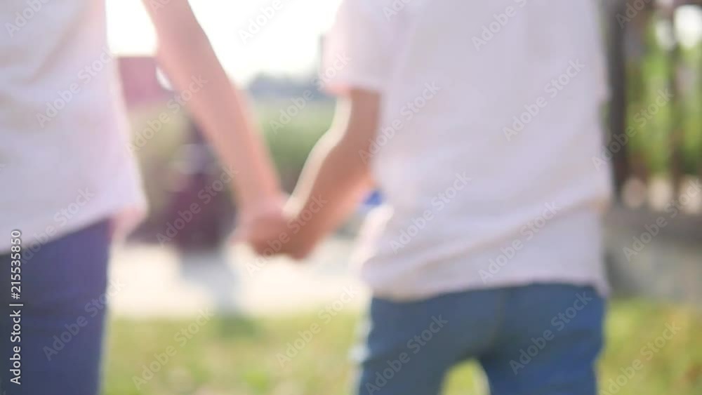 Small children hold their hands, how to run, as far from the camera along the road, a beautiful flash of the lens. Green grass Small children hold their hands, how to run, as far from the camera along the road, a beautiful flash of the lens. Green grass