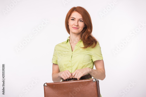 Young happy beautiful ginger woman holding skinny suitcase on white background
