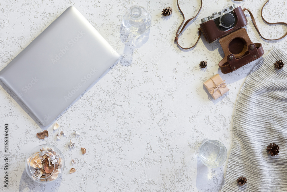 Fototapeta premium Winter flat lay background. Top view of workspace or office desk with laptop, vintage photo camera, blanket, cup of coffee, ginger cookies, cone on textured white background