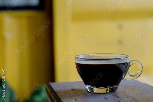 hot Americano coffee or hot black coffee in transparent cup with yellow metal sheet background. have some space for write wording