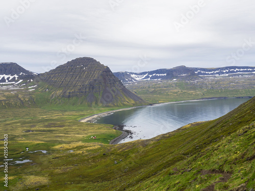 View on beautiful snow covered cliffs and Alfsfell mountain, Hloduvik cove in Hornstrandir, west fjords, Iceland, with river stream, green meadow and abadoned farm budir, moody sky background photo