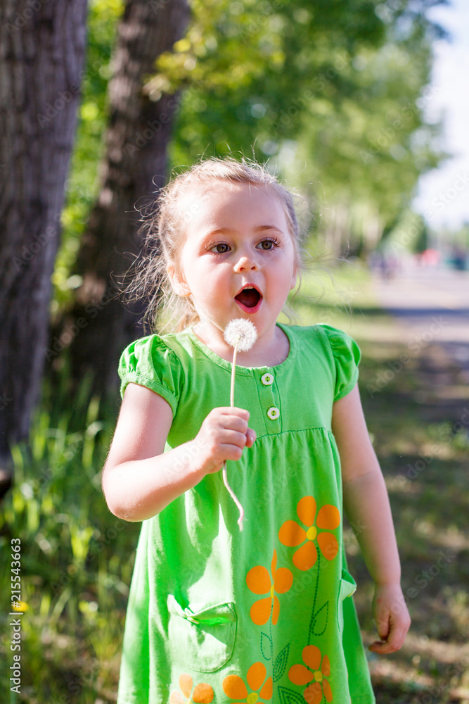 female child in green dress holds dandelion and blows
