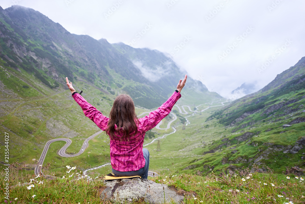 Woman Tourist Sits With Her Arms Wide Open And Looks Up Against woman-tourist-sits-with-her-arms-wide-open-and-looks-up-against