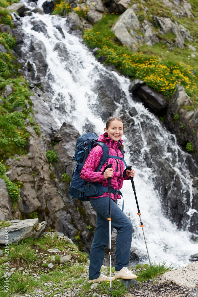 Beautiful woman climber posing on rock near magnificent waterfall. Female tourist green grassy hill spectacular nature view happy healthy sport lifestyle