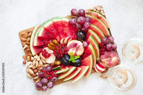 Fruit salad with watermelon, plum, peach, red currant, grape on wooden tray over white background