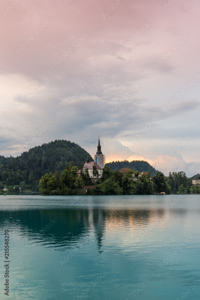 Bled lake with the island and church. Blue water and storm clouds.