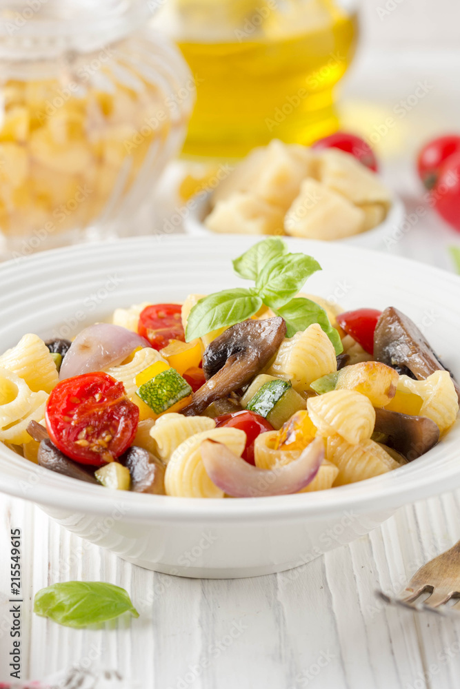 Italian pasta with fried vegetables and mushrooms, zucchini, cherry tomatoes, champignon, cheese and Basil. White plate