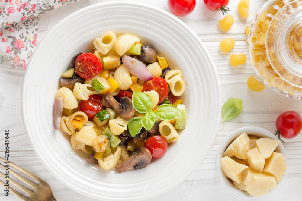 Italian pasta with fried vegetables and mushrooms, zucchini, cherry tomatoes, champignon, cheese and Basil. White plate Italian pasta with fried vegetables and mushrooms, zucchini, cherry tomatoes, champignon, cheese and Basil. White plate
