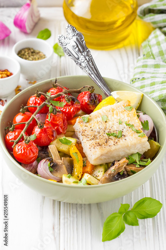 Baked vegetables with mushrooms and white fish fillets in bowl. Zucchini, cherry tomatoes on a branch, red onions, bell peppers and garlic. Healthy diet food