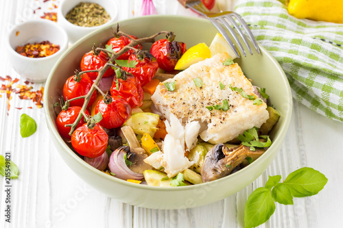 Baked vegetables with mushrooms and white fish fillets in bowl. Zucchini, cherry tomatoes on a branch, red onions, bell peppers and garlic. Healthy diet food