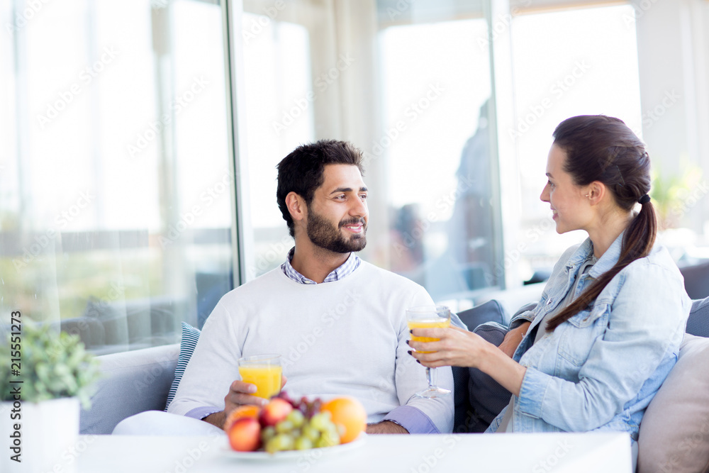 Young couple in casualwear relaxing in hotel cafe, drinking juice and having pleasant talk Young couple in casualwear relaxing in hotel cafe, drinking juice and having pleasant talk