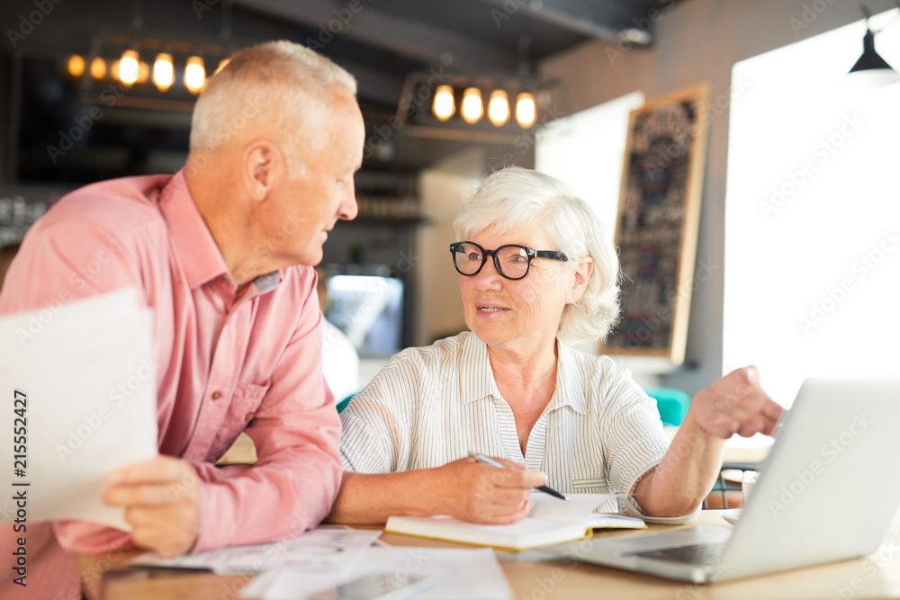 Mature businesswoman explaining her colleague one of working points in laptop or making presentation of project Mature businesswoman explaining her colleague one of working points in laptop or making presentation of project