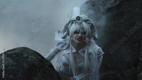 Portrait of a woman dressed as magical creature and posing in the forest. Woman standing between two giant rocks in fog and grinning.