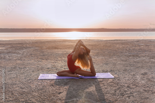 Young girl in nature practicing yoga in a pose Eka Pada Rajakapotasana at sunset 
