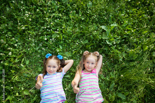 two little beautiful girls lie on green grass in summer park
