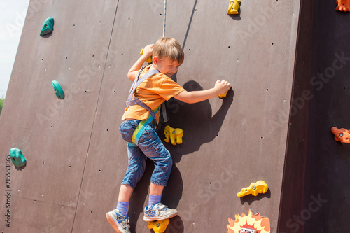 A frightened and happy little boy carrying an artificial rock with a safety rope, is engaged in rock climbing.
