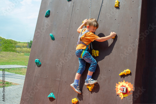 A frightened and happy little boy carrying an artificial rock with a safety rope, is engaged in rock climbing.