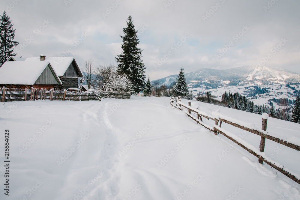 Snow-capped wooden fence, houses in mountains Carpathians Ukraine. On background Christmas tree in forest. Winter nature. Landscape. Top side view. Bukovel. On background of forest and ski slopes.