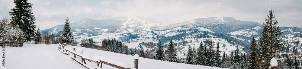 Snow-capped wooden fence in mountains Carpathians Ukraine. On background Christmas tree in forest. Winter nature. Landscape. Top side view. Long edge. Panorama. On background of forest and ski slopes.